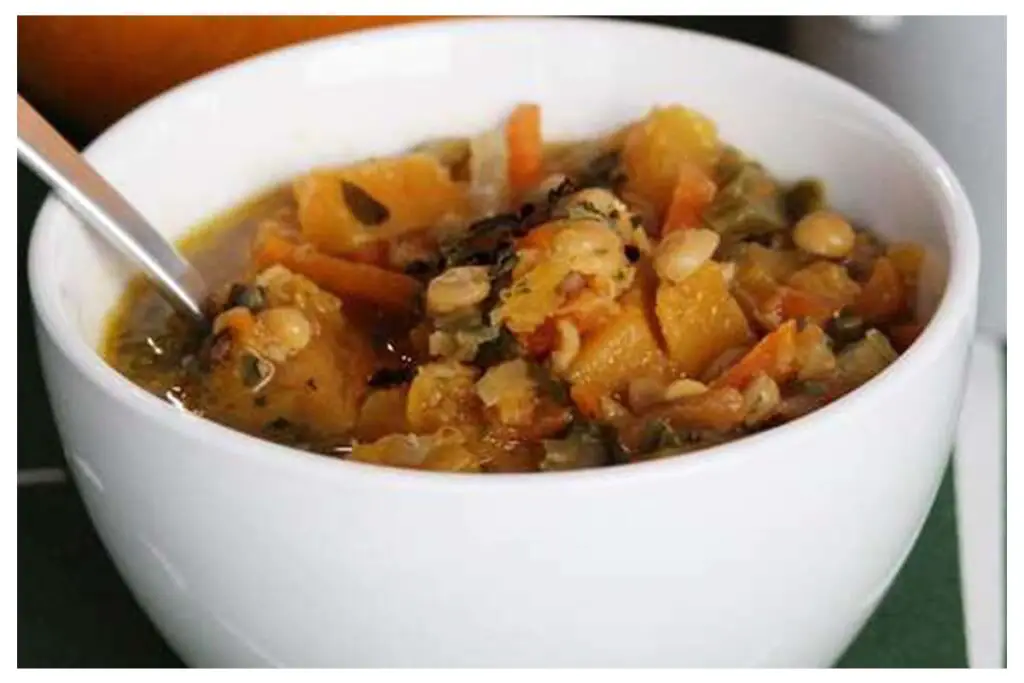 A picture of 30-Minute Squash Coconut Curry in a white bowl with a silver spoon in it.