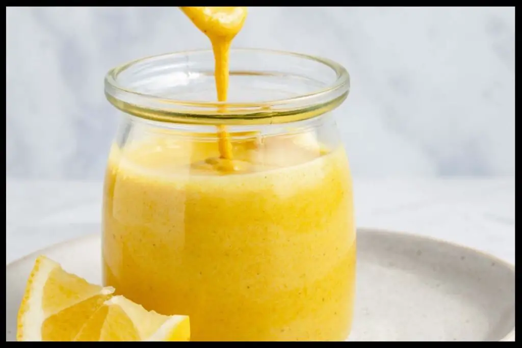 A picture of 5-Minute Sunshine Sauce in a jar on a white plate. A piece of orange is beside it.