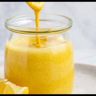 A picture of 5-Minute Sunshine Sauce in a jar on a white plate. A piece of orange is beside it.