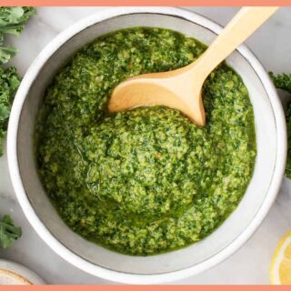 A picture of 5-Minute Vegan Kale Pesto in a white bowl with a wooden spoon in it.