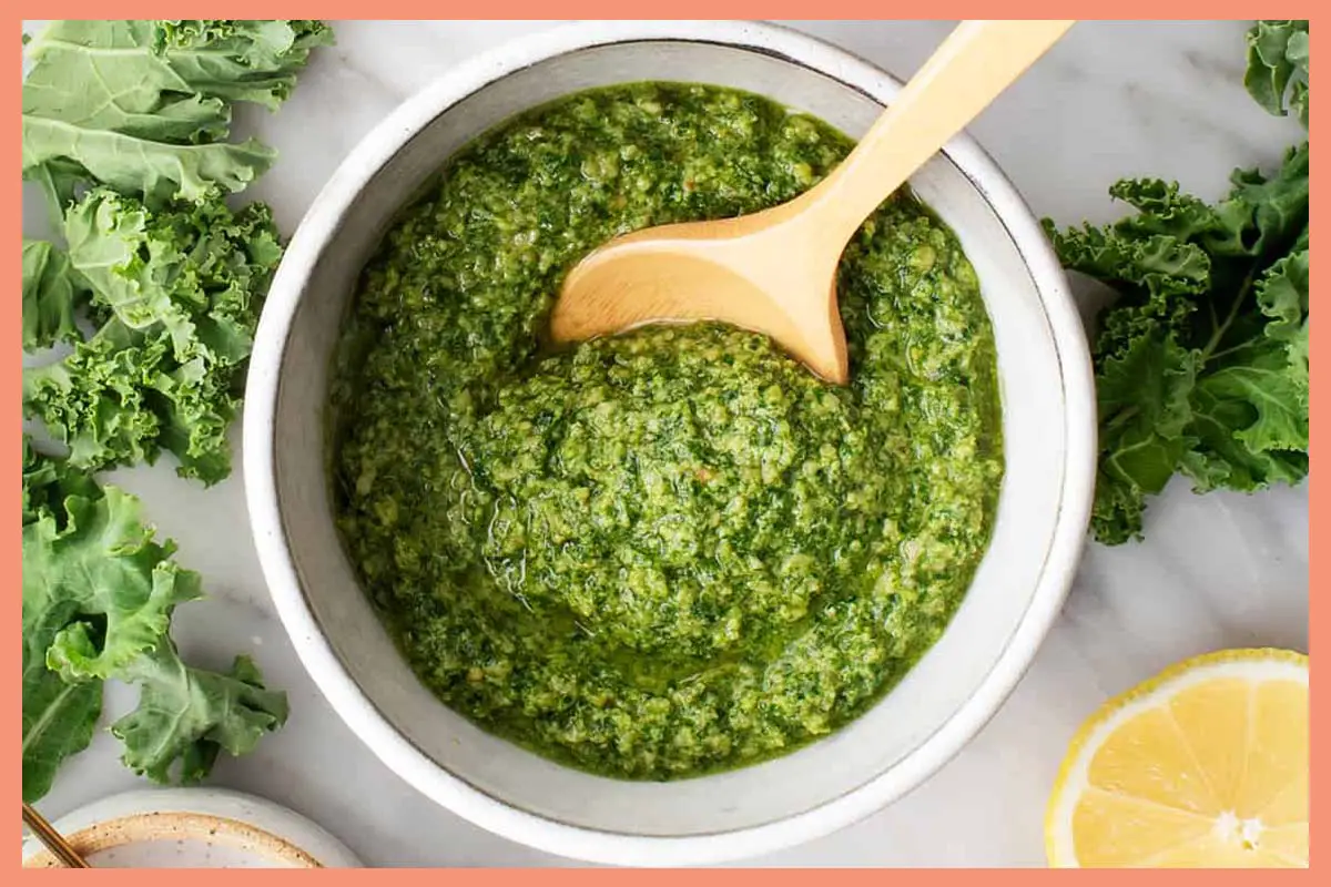 A picture of 5-Minute Vegan Kale Pesto in a white bowl with a wooden spoon in it.