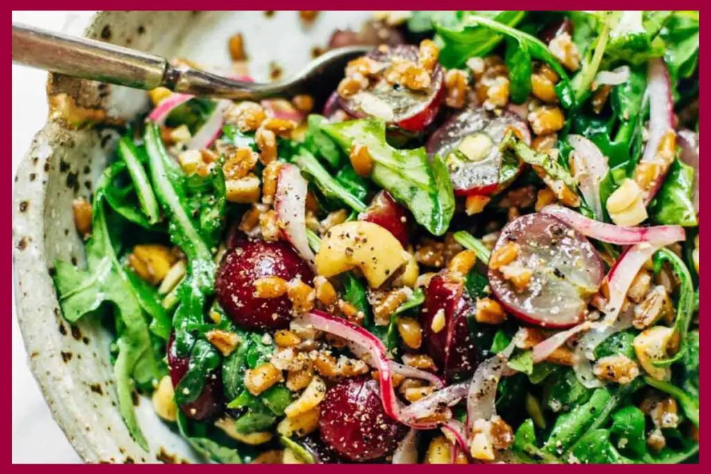 A picture of Arugula Salad With Grapes And Black Pepper Vinaigrette on a plate with a metal spoon in it.