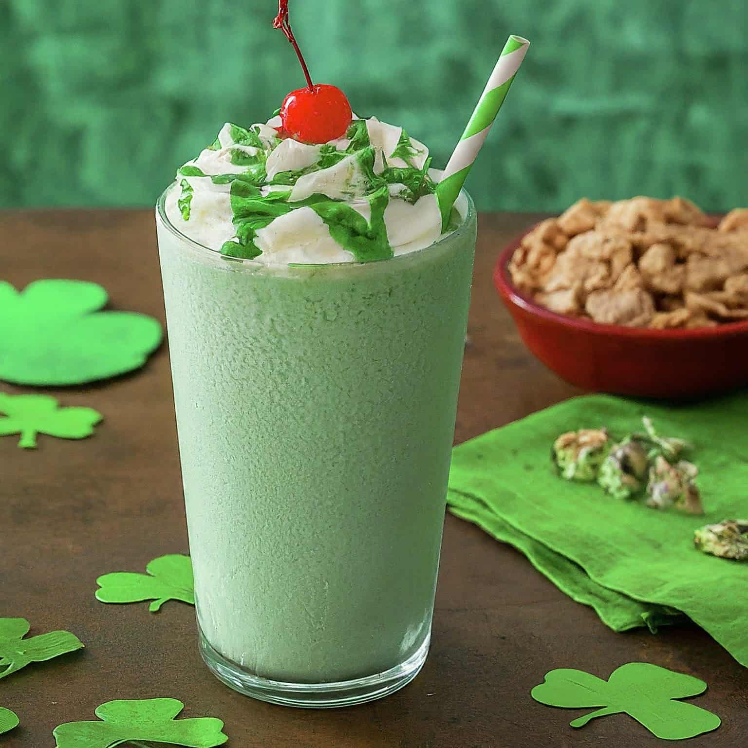Shamrock Shake in a glass cup with a piece of cherry on it and straw inside.
